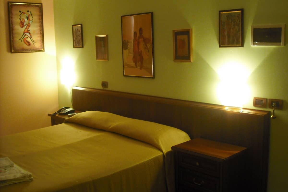 Ein Hotelzimmer mit Bett, Nachttisch und einem an der Wand hängenden Kunstwerk.