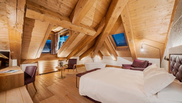 A high-ceilinged room with wooden beams, a bed, a desk, and a chair. - Hotel Royal (Cortina d'Ampezzo)