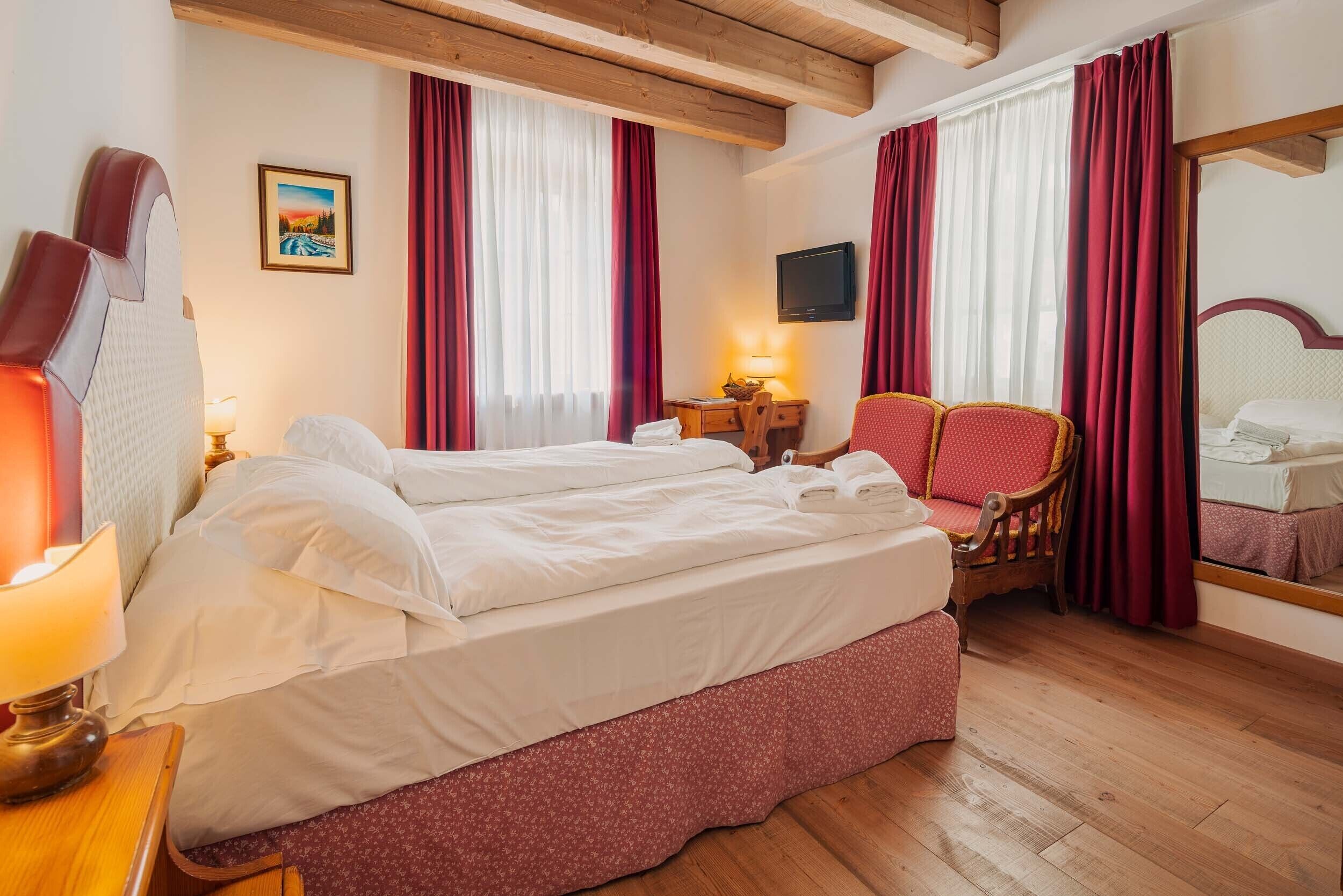 A hotel room with a bed, a desk, a chair, a TV, and a mirror.