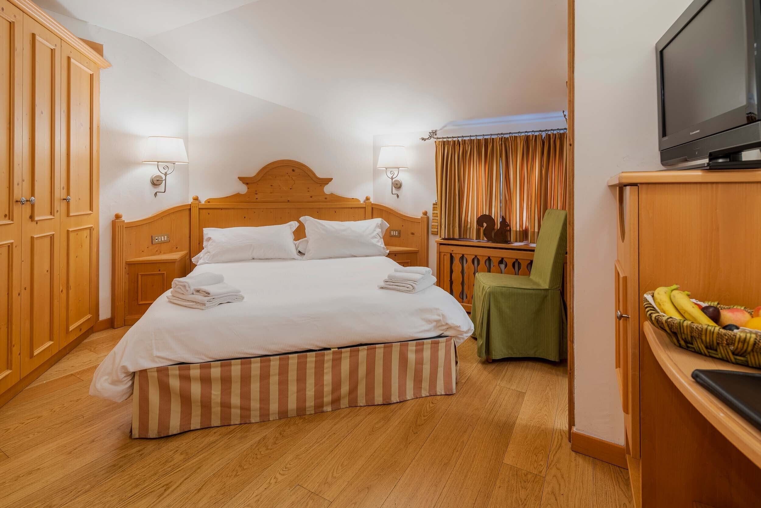 A hotel room with a large bed, wooden wardrobe, a television, and a small table with fruit.