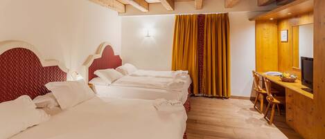 A hotel room with three beds, wooden ceiling beams, a desk with a chair, and a television.