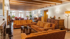A spacious living room with wooden beams, patterned sofas, and a stone fireplace. - Hotel Royal (Cortina d'Ampezzo)