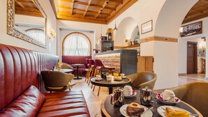 A cozy dining area with leather seating, a round table with breakfast items, and a view of the kitchen in the background. - Hotel Royal (Cortina d'Ampezzo)