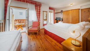 A hotel room with a large bed, a chair, a small table, and a wardrobe. - Hotel Royal (Cortina d'Ampezzo)