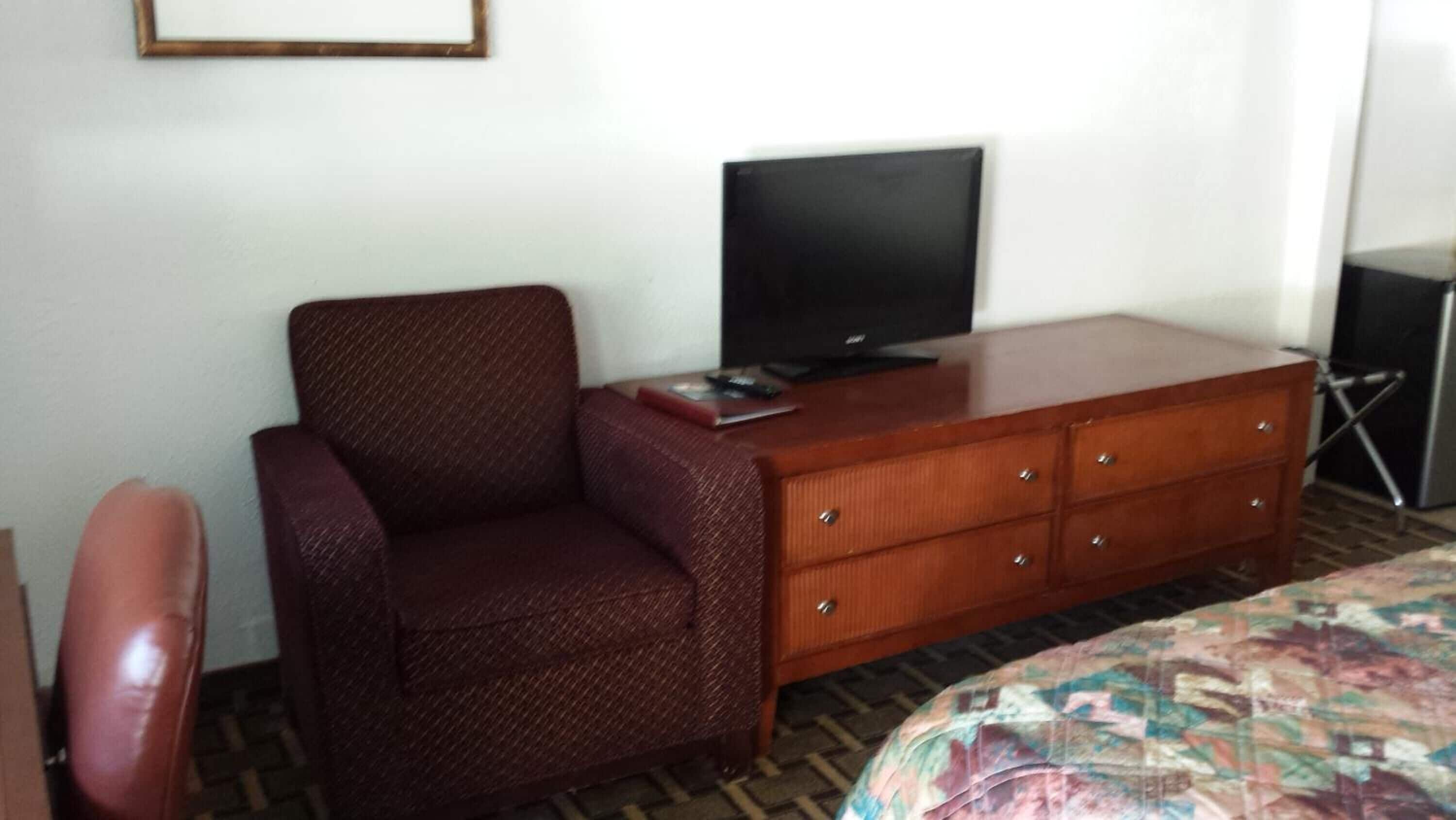 A hotel room with a single bed, a wooden dresser, a television, and a red armchair.