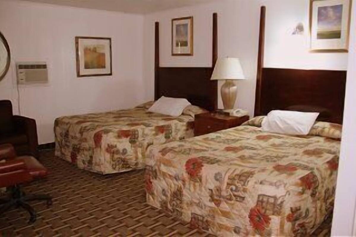 Una habitación de hotel con dos camas, un escritorio, una silla y una lámpara.