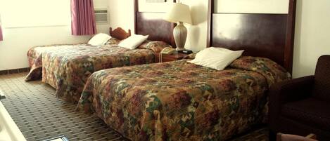 A hotel room with two beds, a desk, a chair, and a lamp.