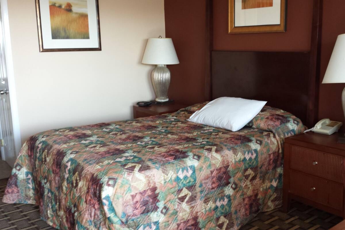 Habitación de hotel con cama, dos lámparas de noche, un teléfono y un cuadro en la pared.