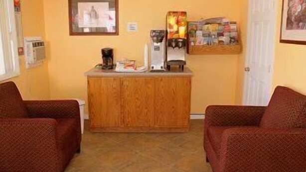 A room with two red patterned chairs, a wooden cabinet with a coffee machine and a small refrigerator, and a wall-mounted shelf with various items.