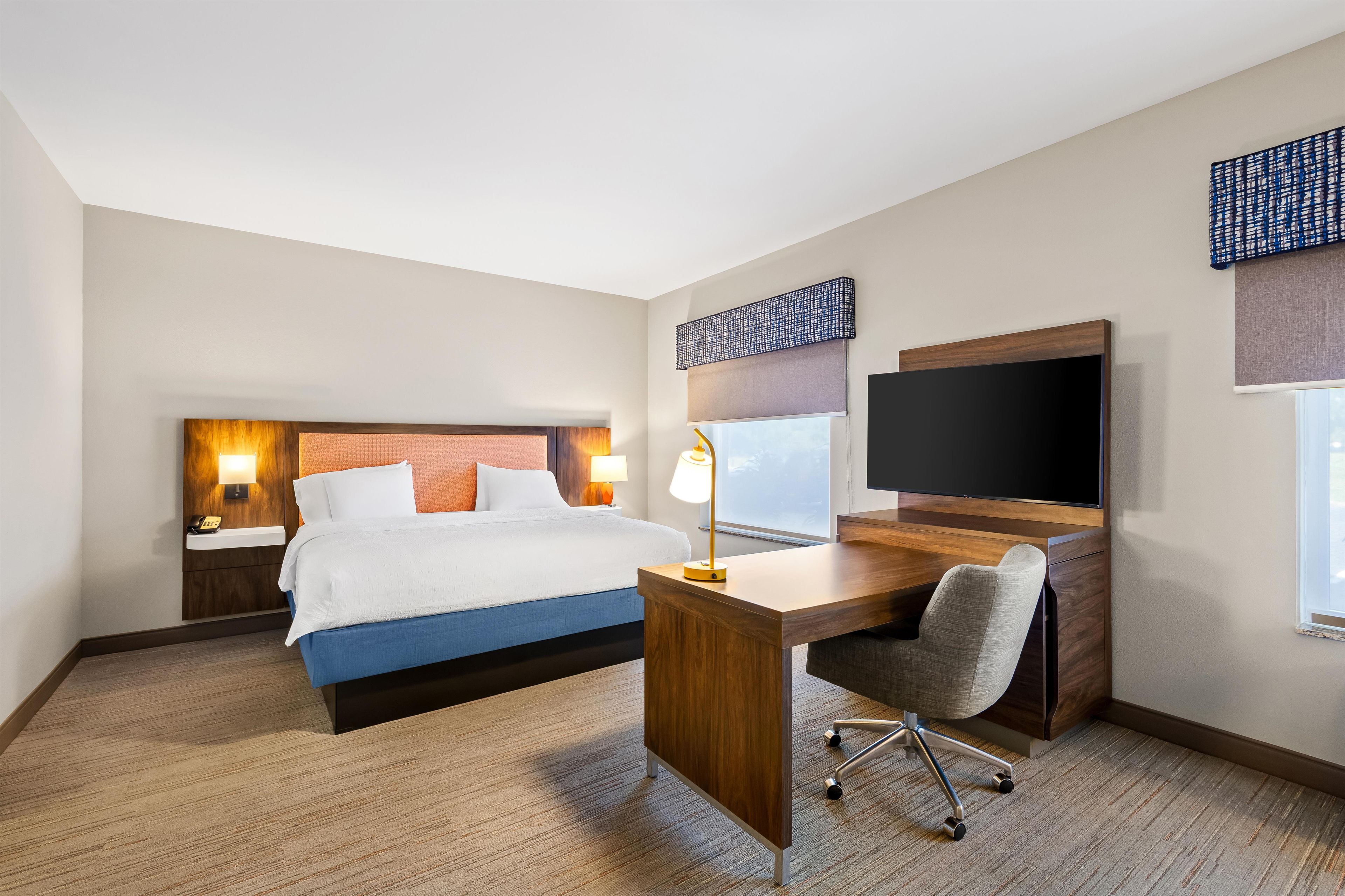 A hotel room with a bed, desk, chair, TV, and two bedside lamps.