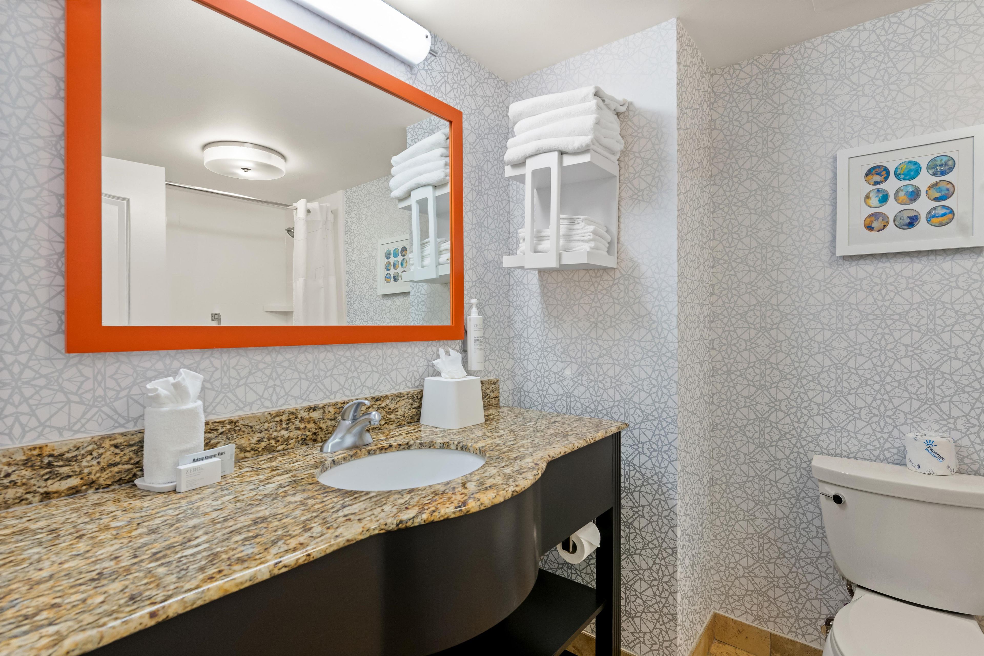 Un baño con encimera de granito, un lavabo blanco, un mueble de tocador negro, un inodoro blanco y un espejo con marco naranja.