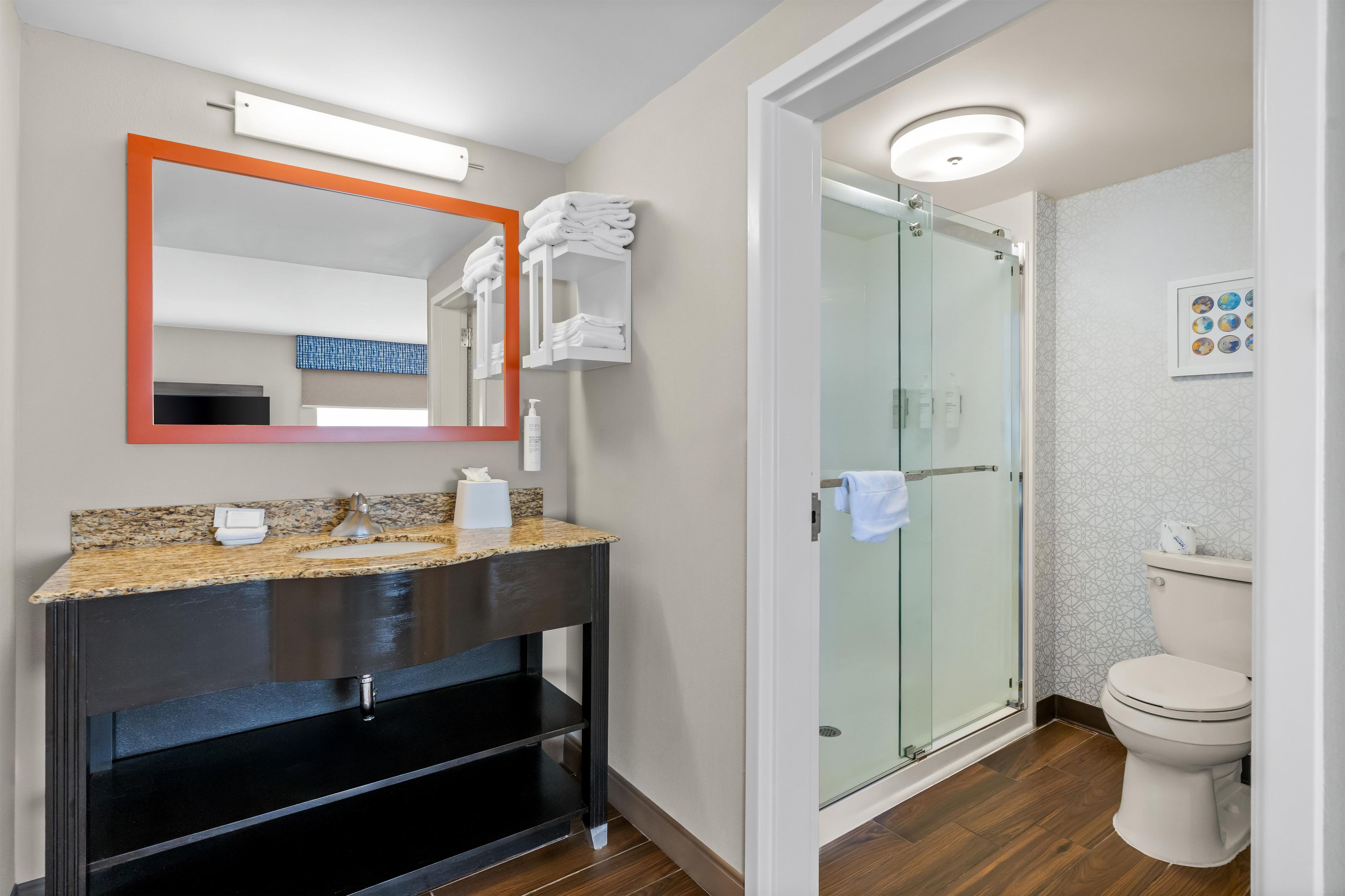 A modern bathroom with a granite countertop, a black vanity, a glass shower enclosure, and a toilet.