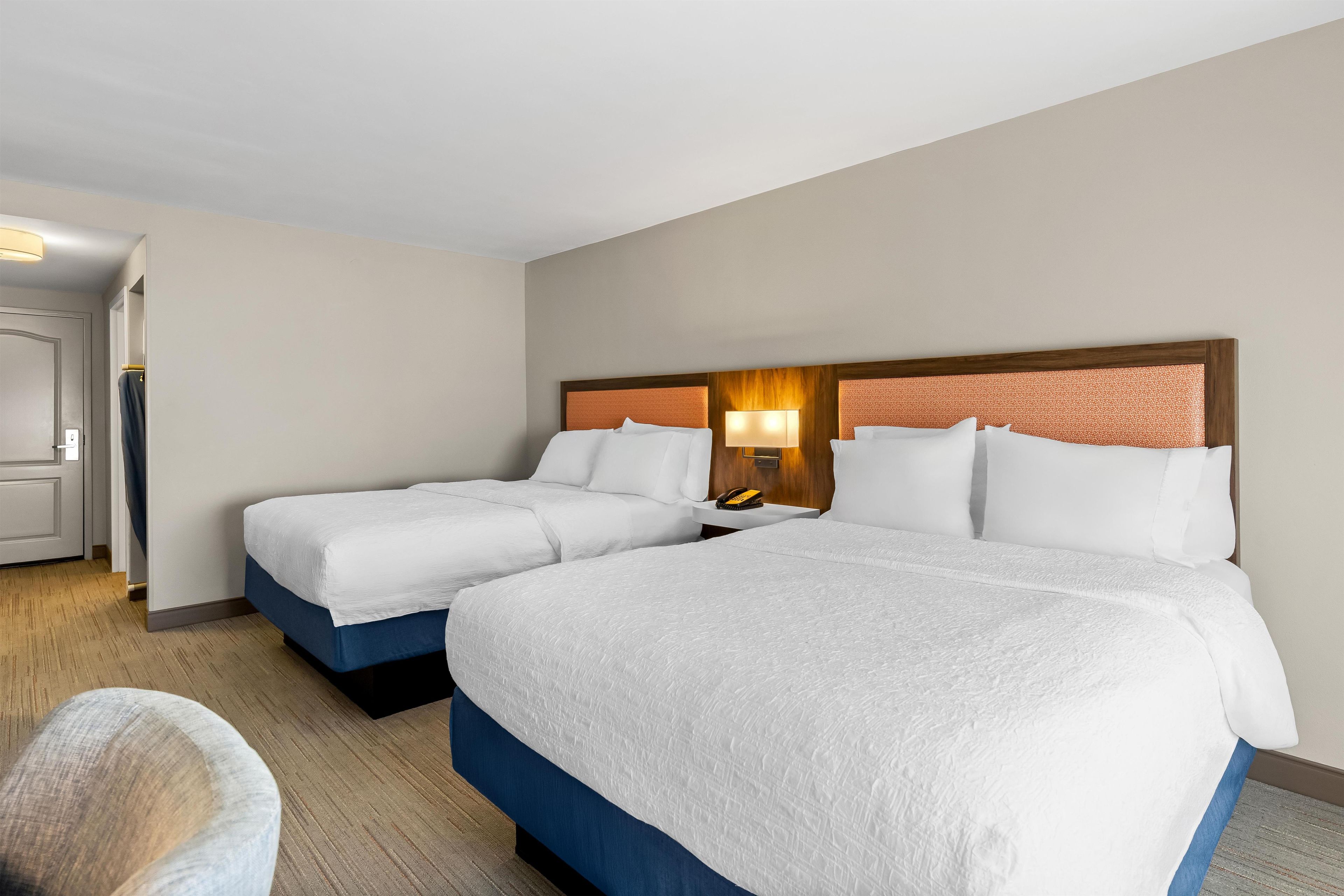 A hotel room with two beds, a desk, and a chair.