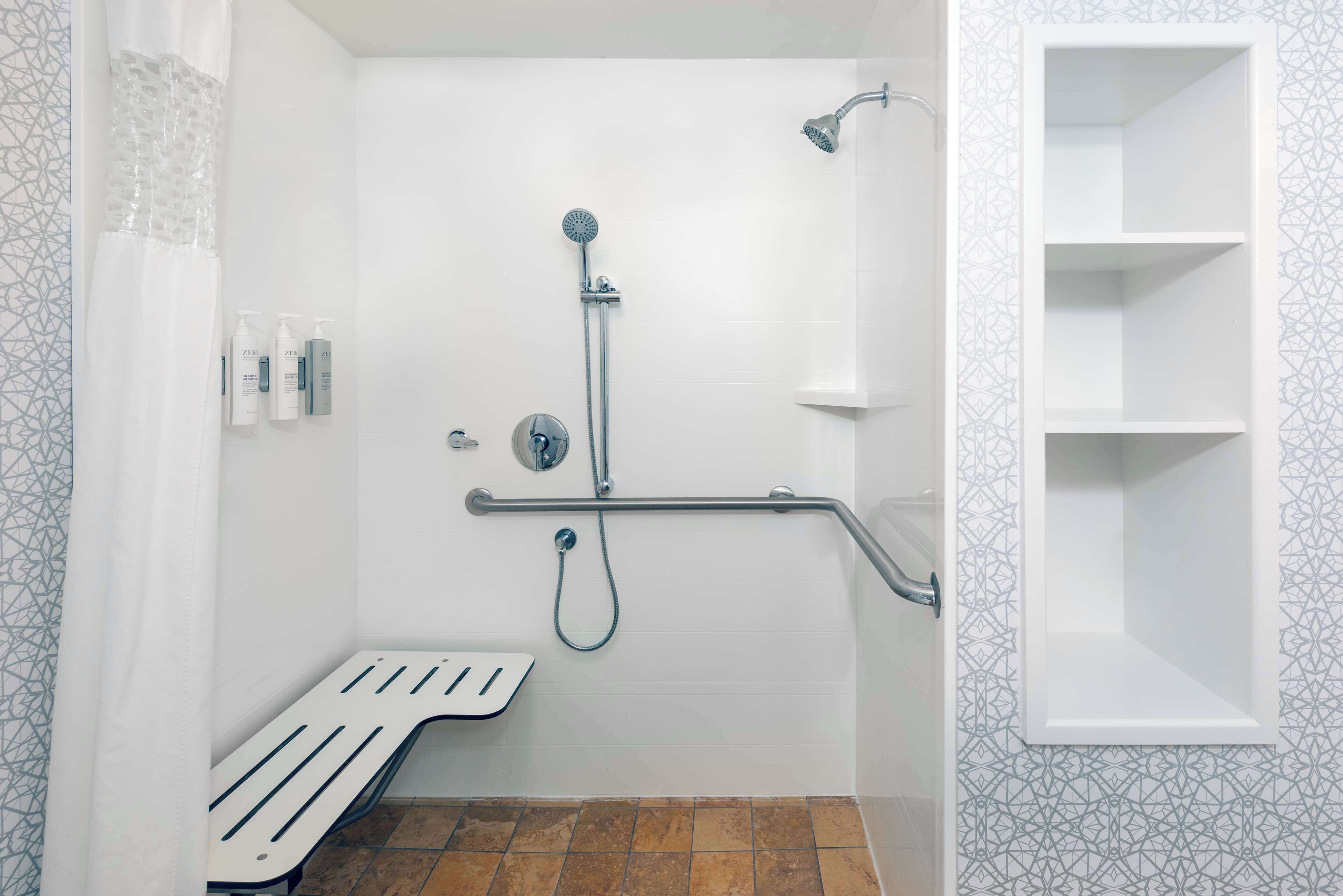A bathroom with a shower, a handrail, a shelf, and a bench.