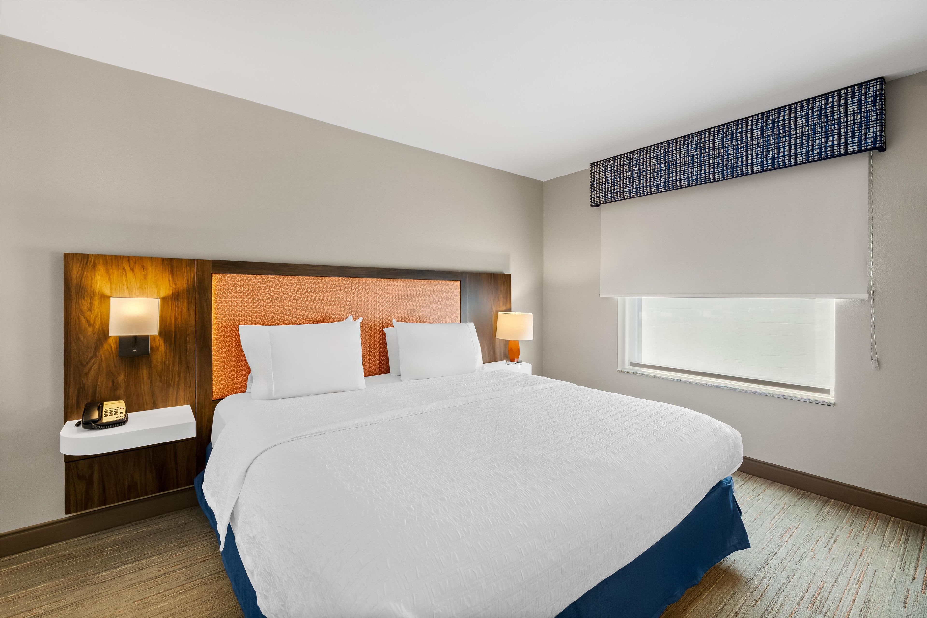 A hotel room with a large bed, two bedside lamps, a telephone, and a window with blinds.