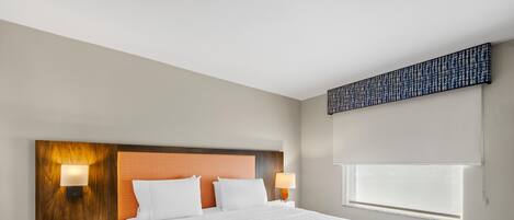 A hotel room with a large bed, two bedside lamps, a telephone, and a window with blinds.