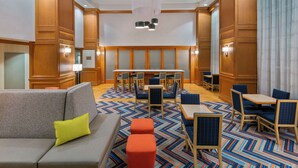 A hotel lobby with a central dining area, sofas, and a patterned carpet.