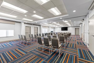 A conference room with rows of chairs, a carpeted floor, and a flat-screen TV on the wall.