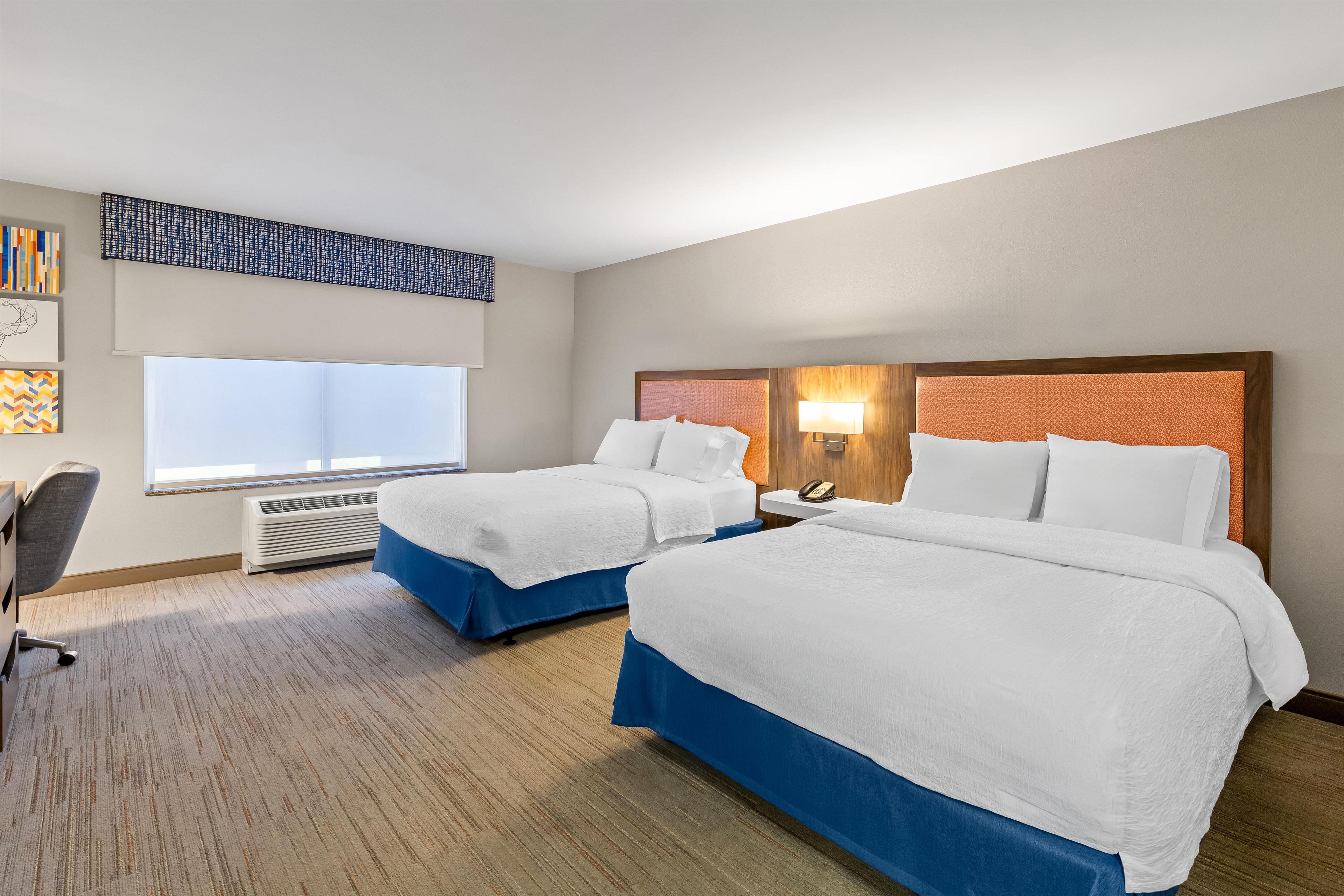 Habitación de hotel con dos camas, un escritorio, una silla, un ventanal y un teléfono instalado en la pared.