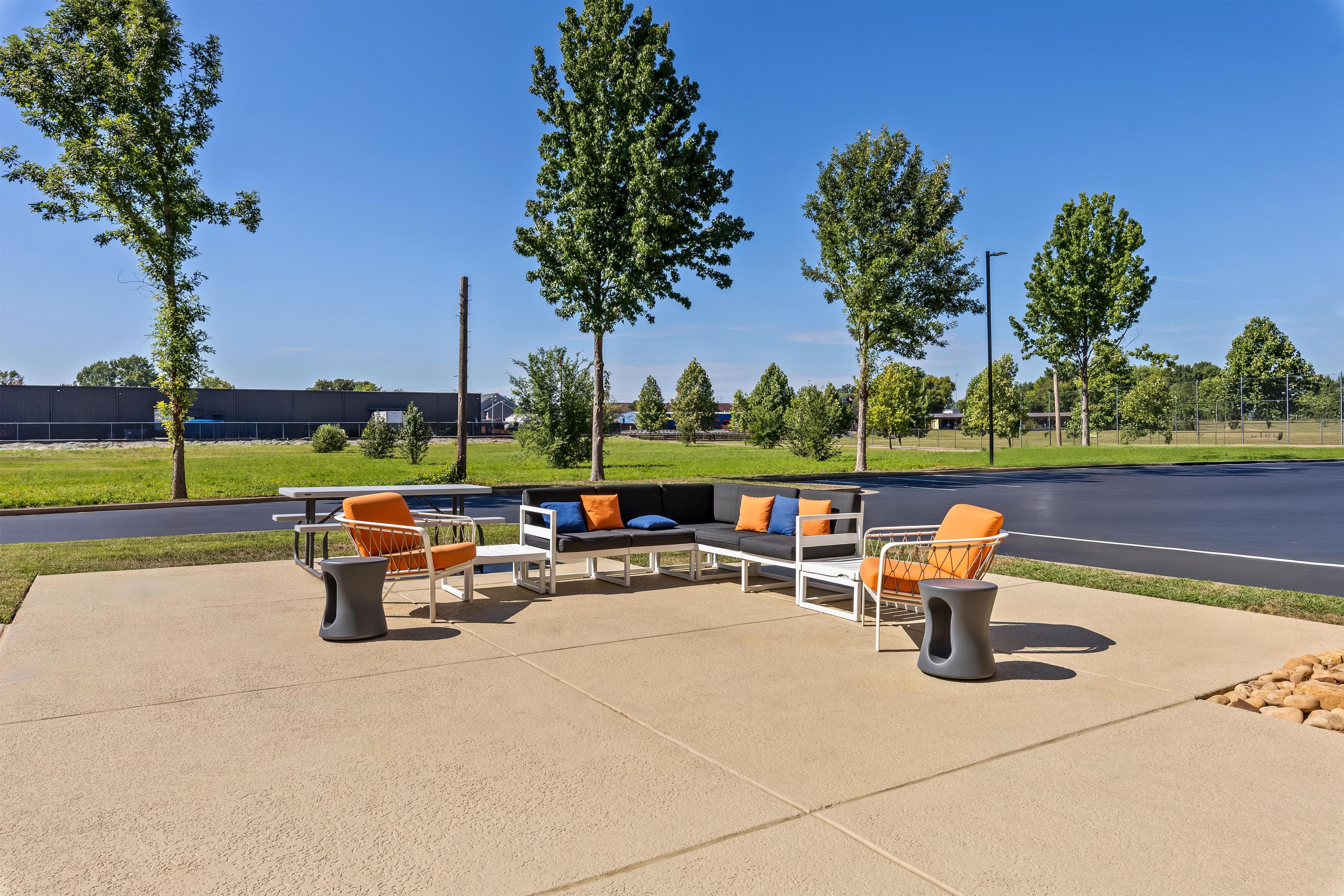 An outdoor seating area with a sectional sofa and chairs, surrounded by trees and a clear sky.