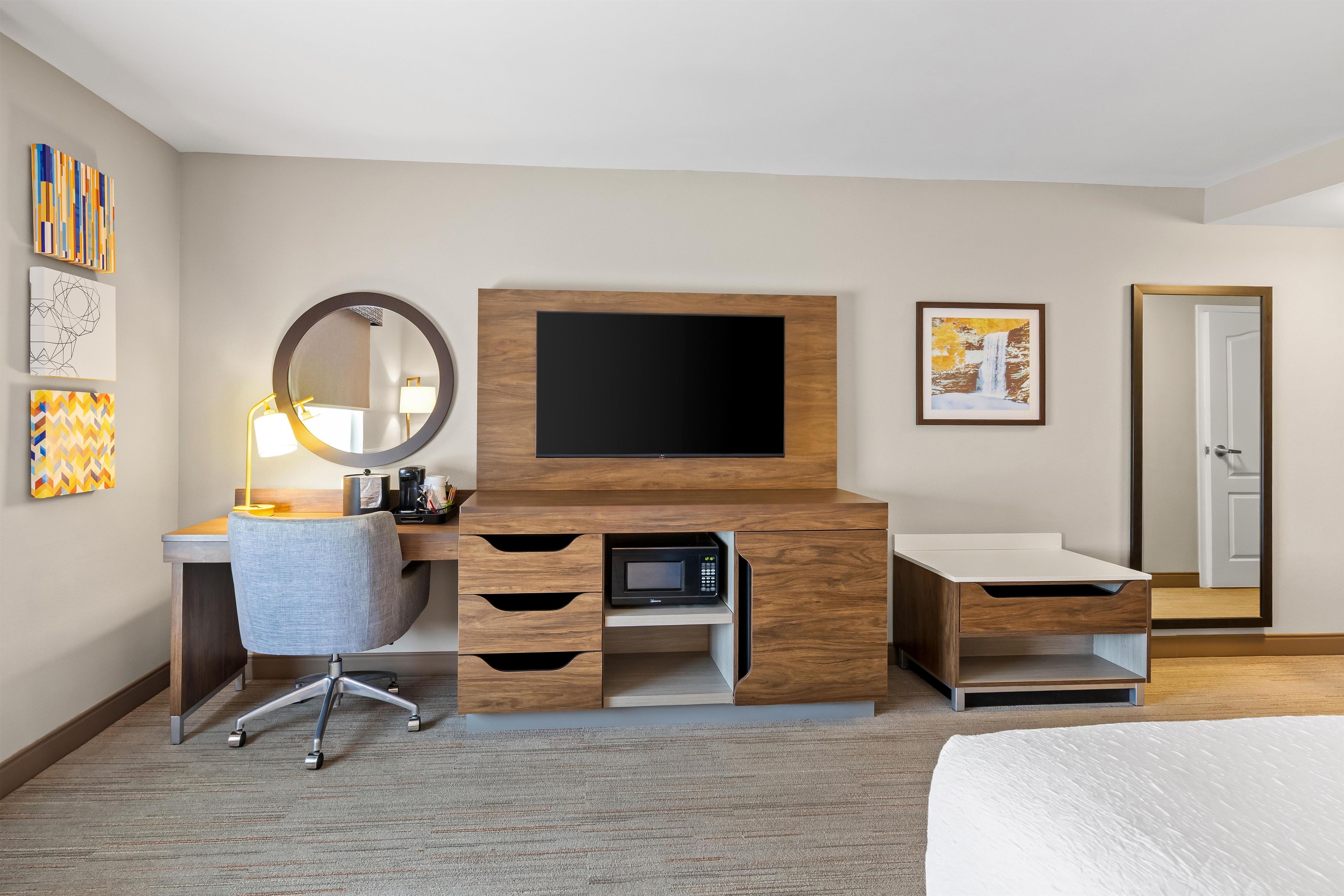 A hotel room with a wooden desk, a flat-screen TV, a chair, a microwave, and a bed.