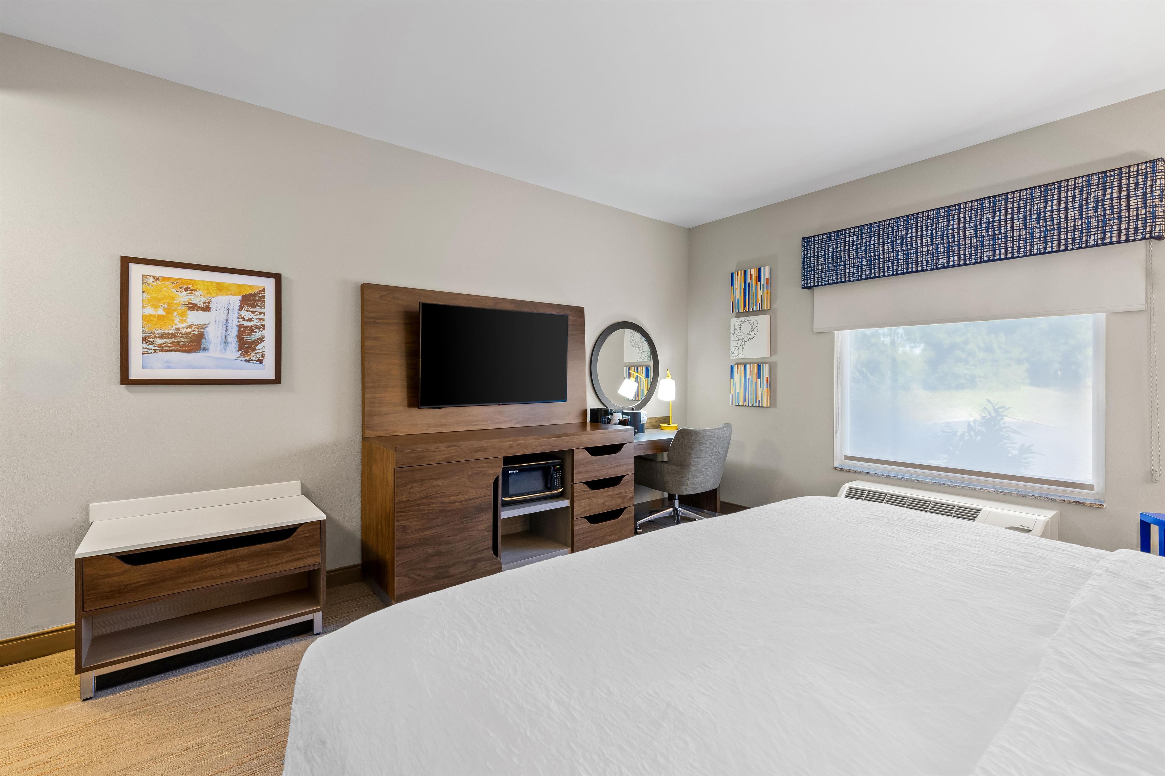 Een hotelkamer met een bed, een bureau met een flatscreen televisie, een magnetron, een stoel, een dressoir en kunstwerken aan de muren.