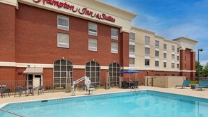 A Hampton Inn & Suites with a swimming pool, outdoor seating, and a brick facade.