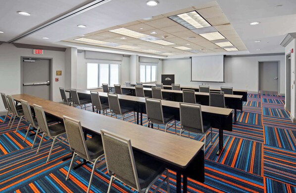 A conference room with a long table, chairs, a projector screen, and a carpeted floor.