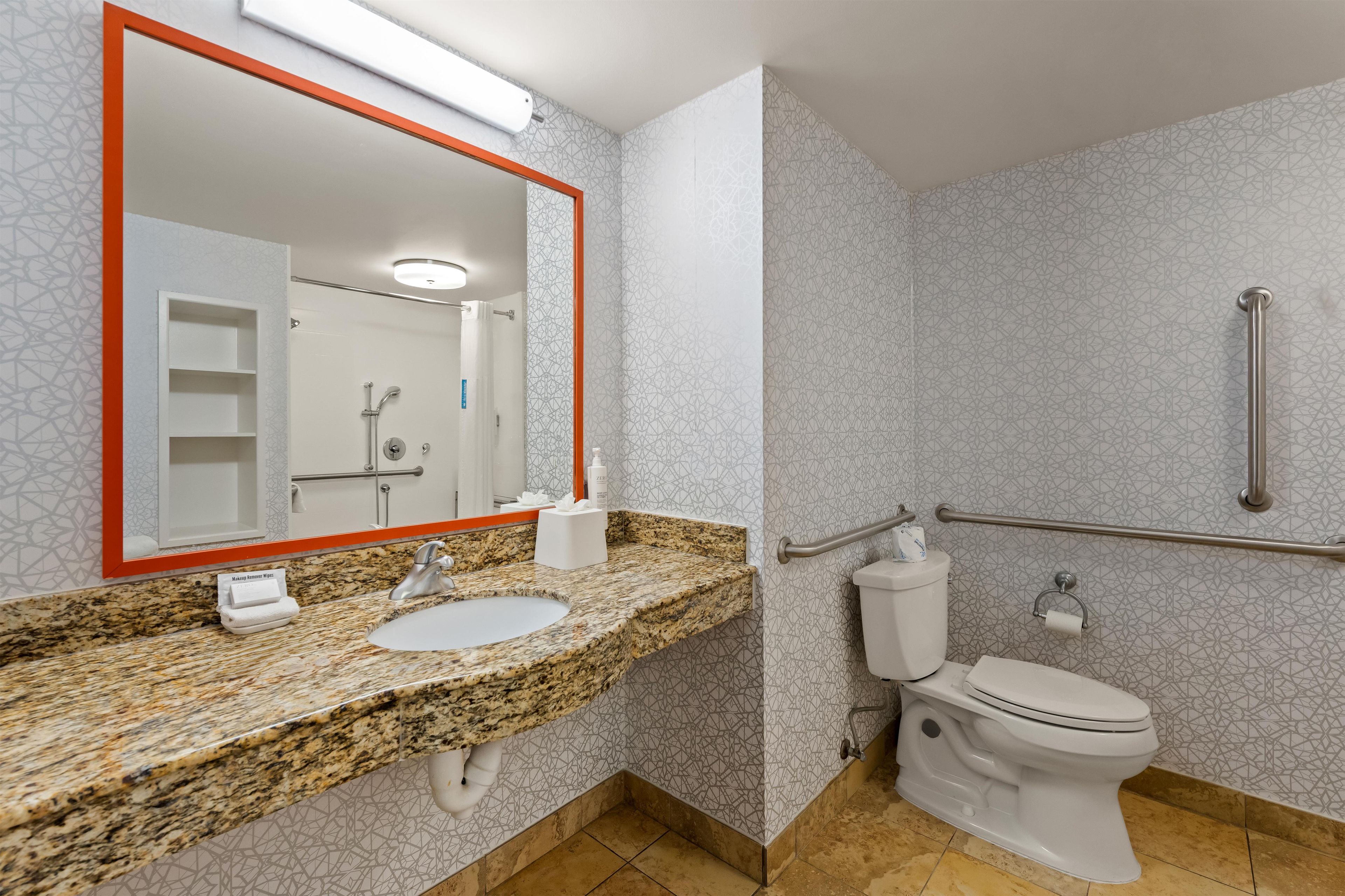 A bathroom with a granite countertop, a sink, a toilet, and a shower area.