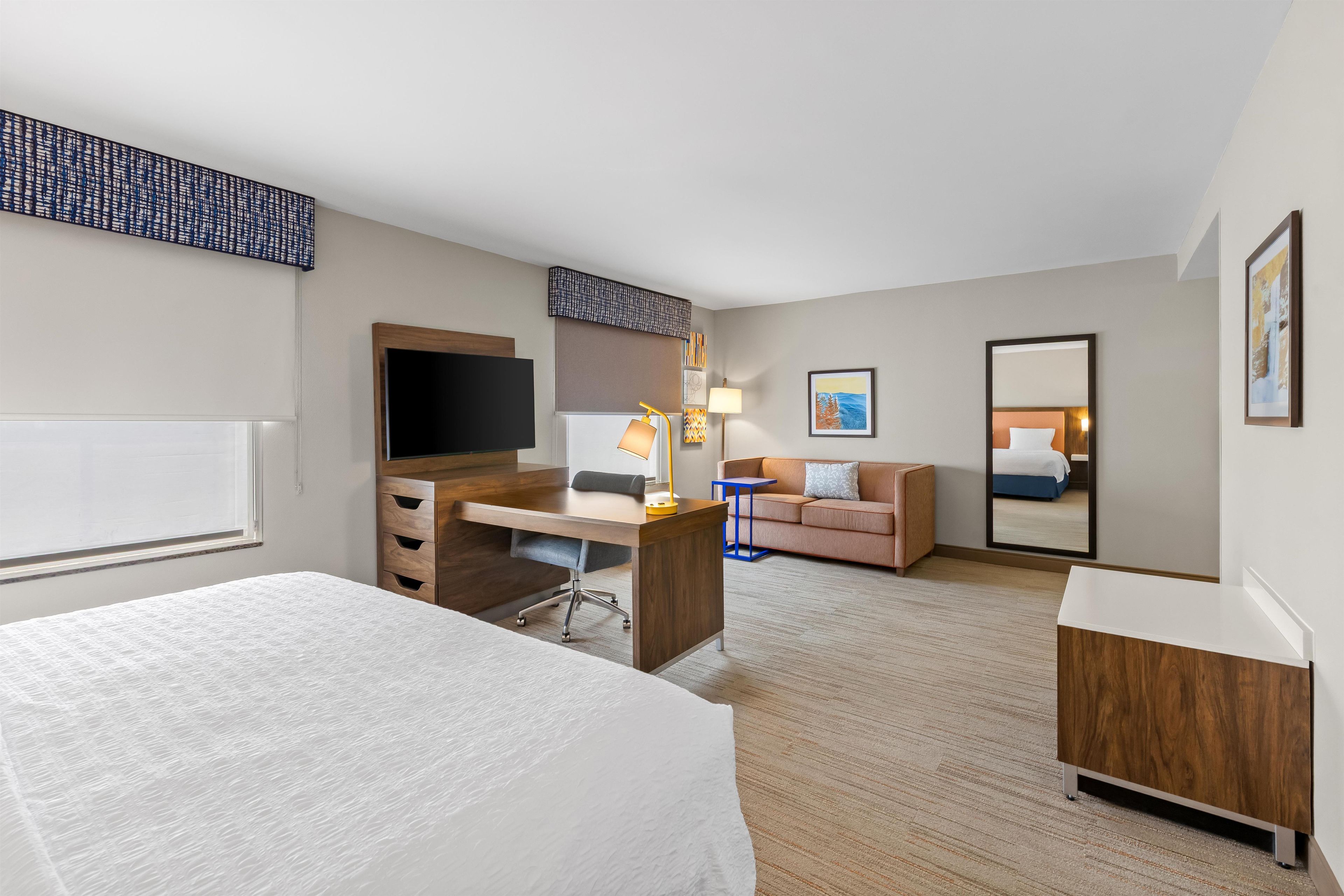 A hotel room with a bed, desk, chair, sofa, and a mirror.