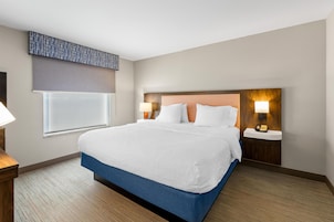 Habitación de hotel con una cama grande, dos mesitas de noche, una ventana con persiana y un teléfono instalado en la pared.