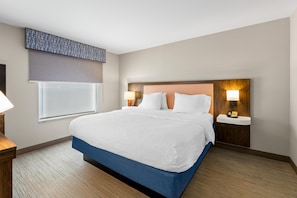 A hotel room with a large bed, two bedside tables, a window with a blind, and a wall-mounted telephone.