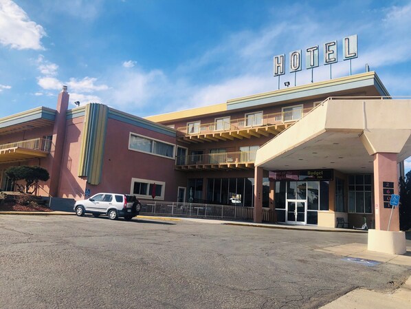 A hotel with a prominent 'HOTEL' sign, a covered entrance, and a parking area with a white car.
