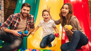 Une famille dans un parc avec un toboggan et des balles colorées.