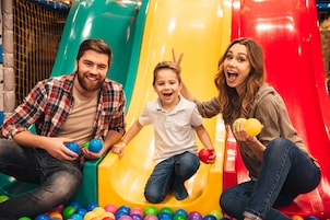 Una familia en un parque infantil, con un tobogán y pelotas de colores.