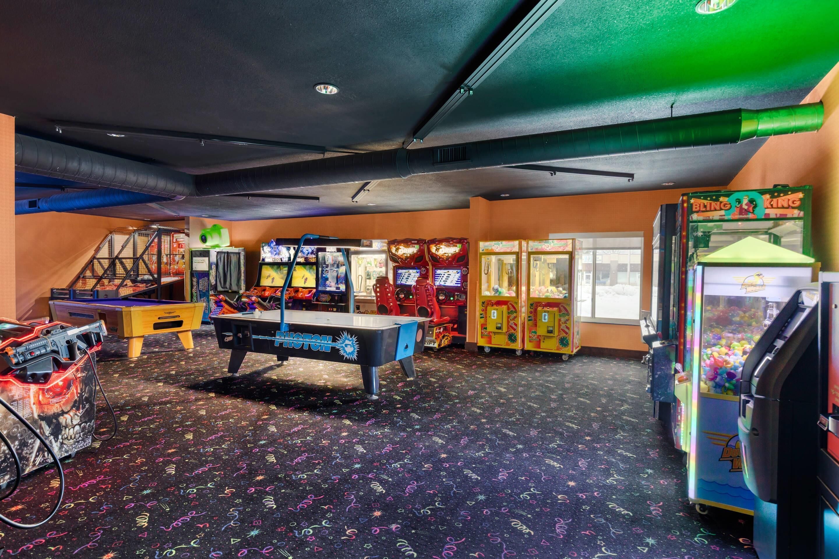 A room with arcade games, a pool table, and a claw machine.