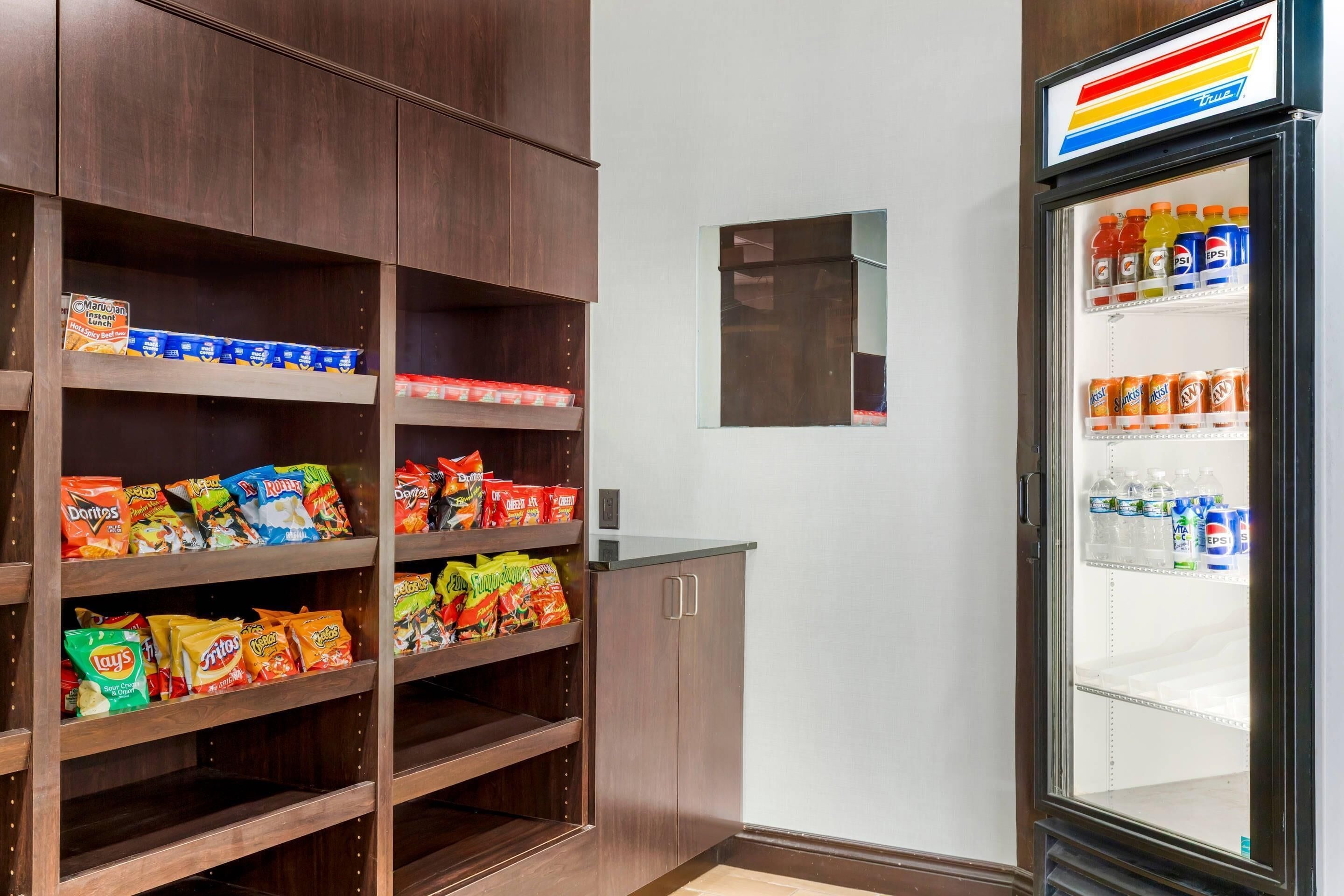 Estante con botanas como papas fritas y un refrigerador con Pepsi y otras bebidas.