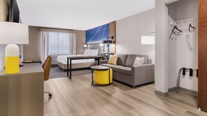 A modern hotel room with a bed, a sofa, a desk, and a small table.