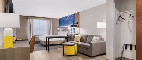 A modern hotel room with a bed, a sofa, a desk, and a small table.