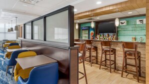Un espace bar d’hôtel avec des sièges, un panneau publicitaire Pepsi et un comptoir bien garni de différentes bouteilles.