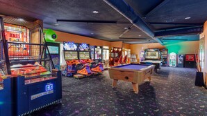 Un espace de loisirs intérieur comprenant des jeux d’arcade, une table de billard et une table de snooker.