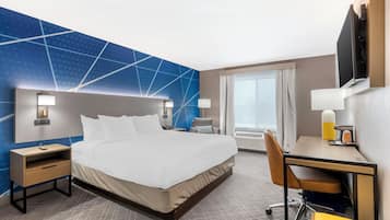 A hotel room with a large bed, a desk, a chair, a nightstand, and a TV.