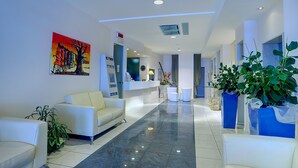 A modern hotel lobby with a reception desk, seating area, and decorative plants. - Hotel Cristallo Riccione (Riccione)
