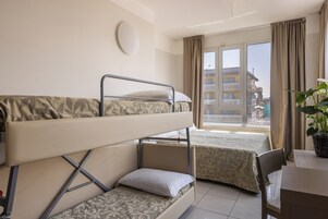 A hotel room with bunk beds, a dining table, a potted plant, and a window with a view of buildings.