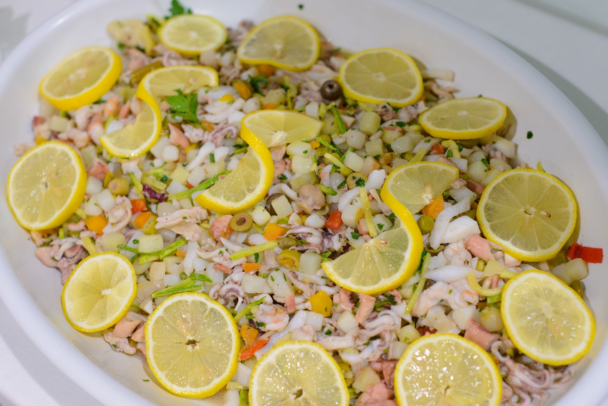A white plate with a seafood salad topped with lemon slices.