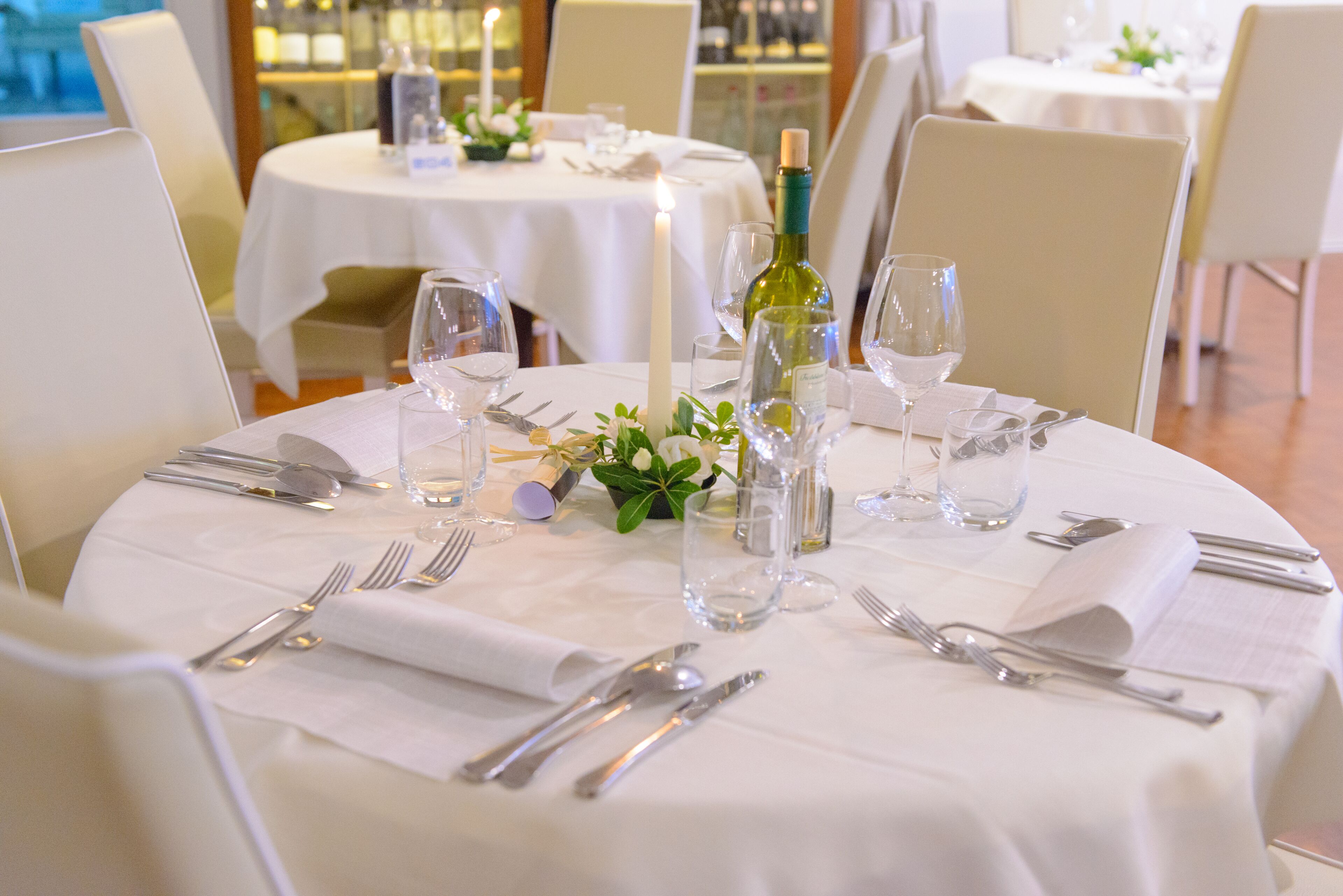 Une table dressée pour le dîner, avec une nappe blanche, des couverts en argent et une bouteille de vin.