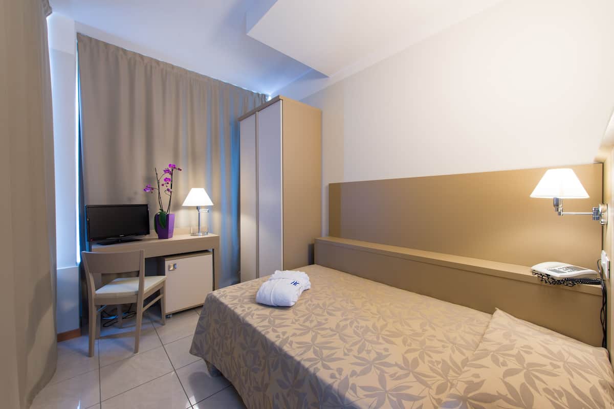 A hotel room with a bed, a desk with a TV, a chair, and a lamp.