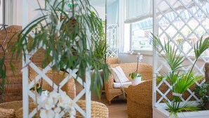 A wicker lounge area with a sofa and chairs, surrounded by potted plants and a white lattice partition. - Hotel Cristallo Riccione (Riccione)