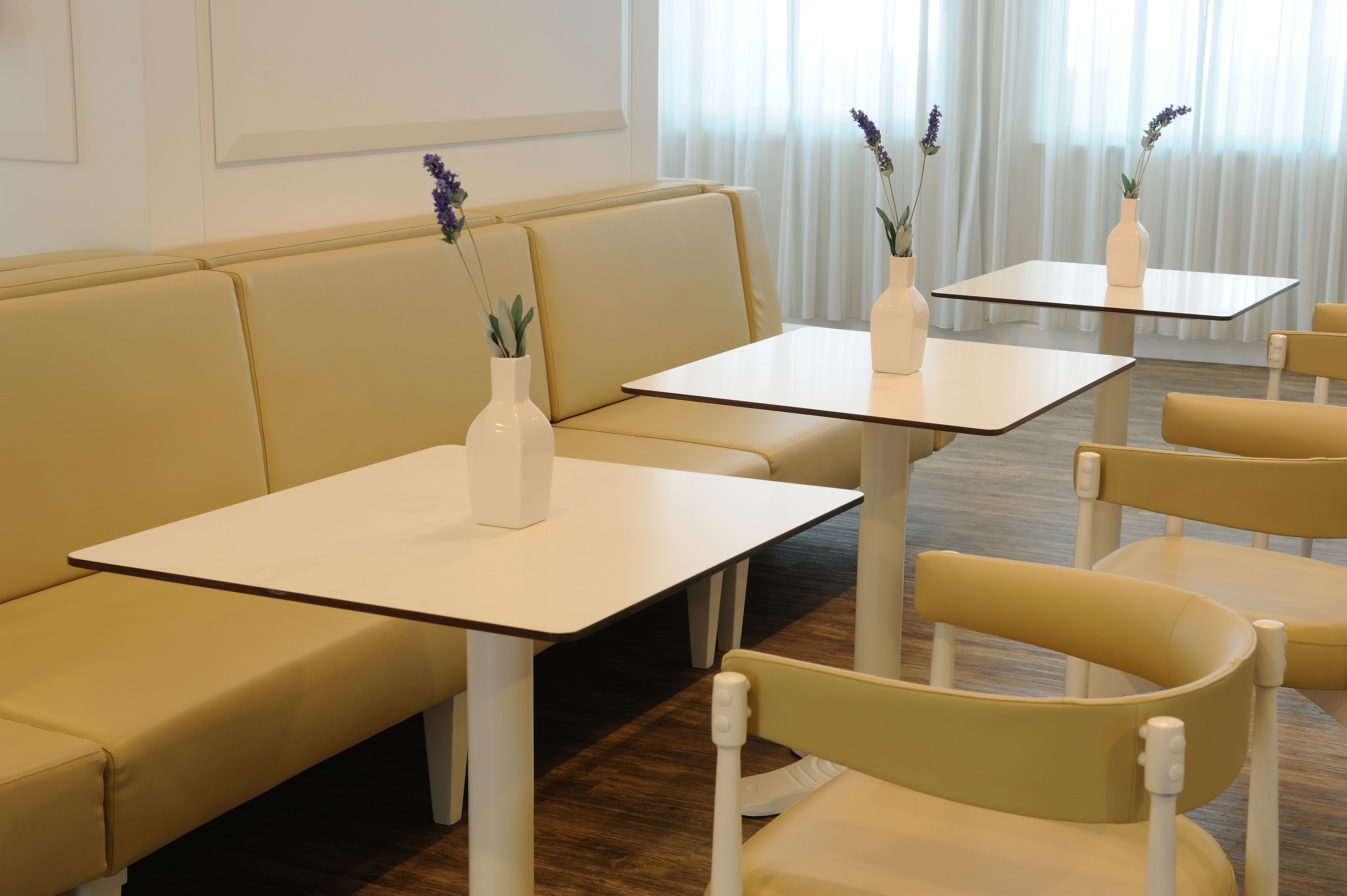 Une pièce moderne et bien éclairée, avec un canapé jaune, des tables blanches et des chaises assorties.