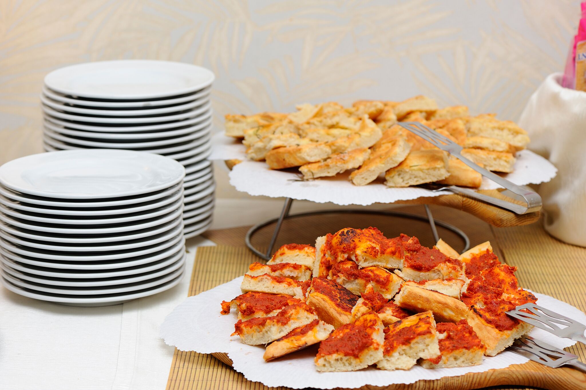 Una mesa con platos blancos apilados y una bandeja de pizza en porciones.
